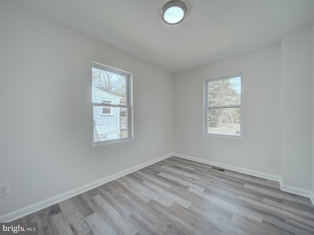 spare room featuring wood finished floors, visible vents, baseboards, and plenty of natural light