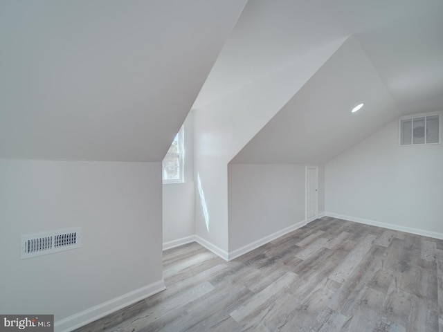 additional living space with vaulted ceiling, wood finished floors, visible vents, and baseboards