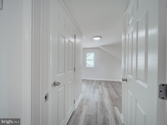 hallway with light wood finished floors, vaulted ceiling, and baseboards