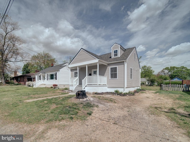 view of front of house with a shingled roof, a front lawn, covered porch, and fence