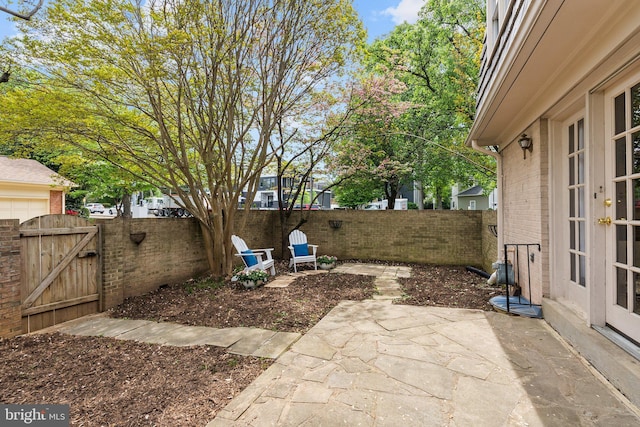 view of yard featuring a patio, french doors, a fenced backyard, and a gate