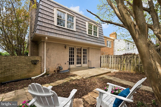 back of property featuring a fenced backyard, brick siding, a patio, mansard roof, and french doors