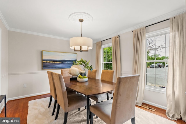 dining space with ornamental molding, light wood finished floors, visible vents, and baseboards