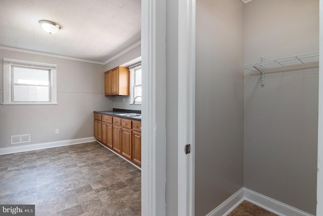 interior space with a sink, dark countertops, visible vents, crown molding, and brown cabinetry