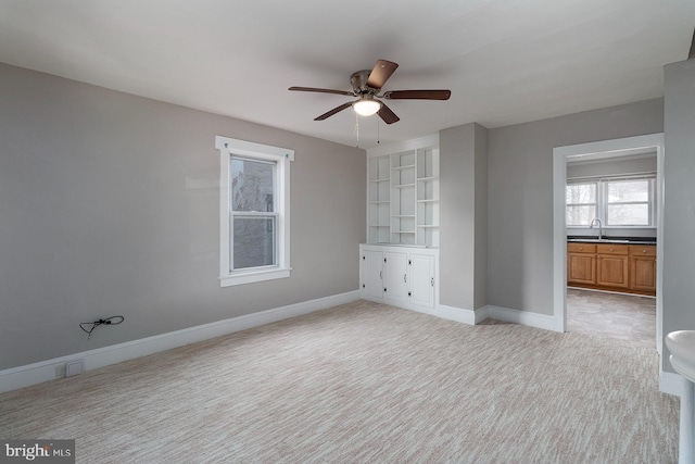 unfurnished room with baseboards, light colored carpet, a sink, and ceiling fan