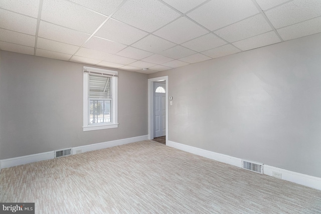 carpeted empty room with baseboards, visible vents, and a drop ceiling