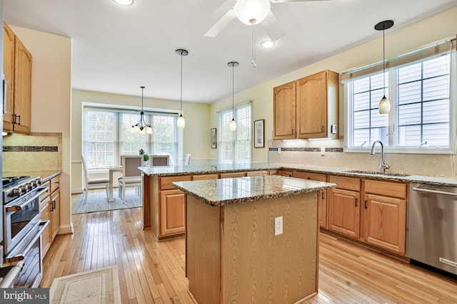 kitchen featuring appliances with stainless steel finishes, a sink, a peninsula, a kitchen island, and light wood finished floors