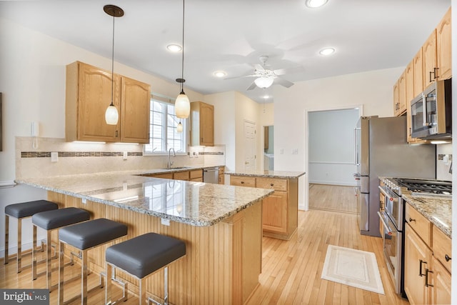 kitchen featuring appliances with stainless steel finishes, a sink, a ceiling fan, a peninsula, and decorative backsplash