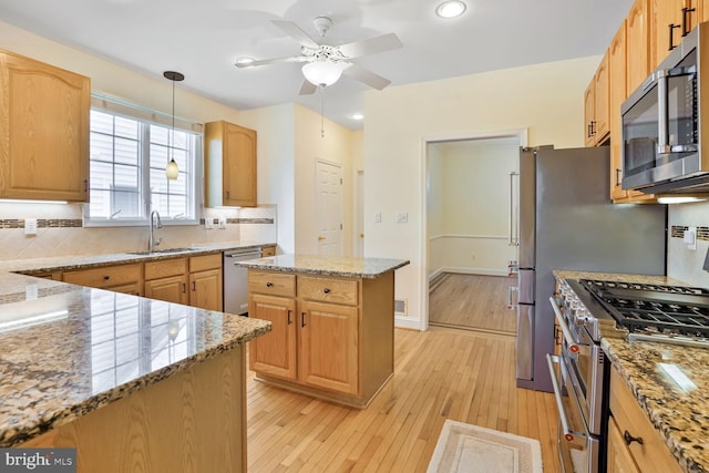 kitchen featuring appliances with stainless steel finishes, a sink, a ceiling fan, tasteful backsplash, and light stone countertops