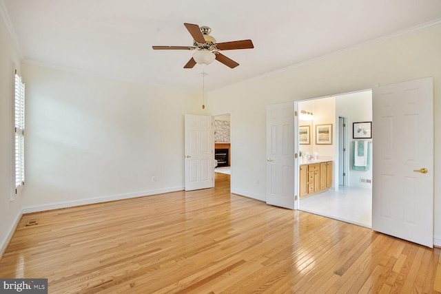 unfurnished bedroom with light wood-style flooring, ornamental molding, baseboards, a fireplace, and ensuite bathroom