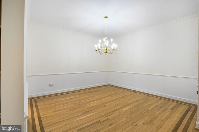 empty room with wood finished floors, a chandelier, ornamental molding, and baseboards