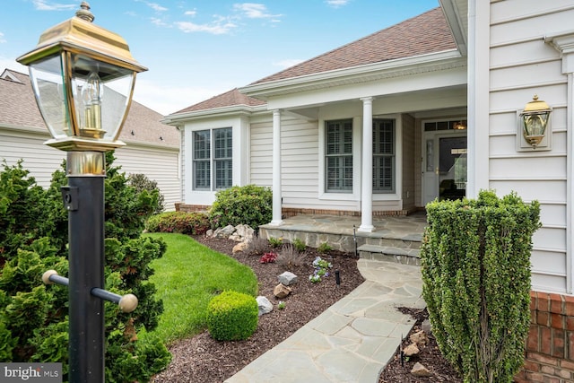 doorway to property with covered porch and a shingled roof