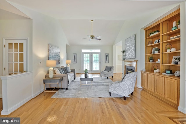 living area featuring a fireplace, light wood-style flooring, a ceiling fan, vaulted ceiling, and baseboards