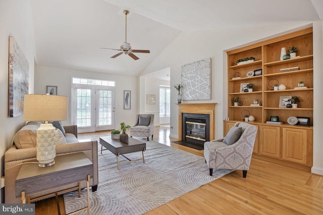 living room featuring light wood-type flooring, a fireplace with flush hearth, a ceiling fan, and high vaulted ceiling