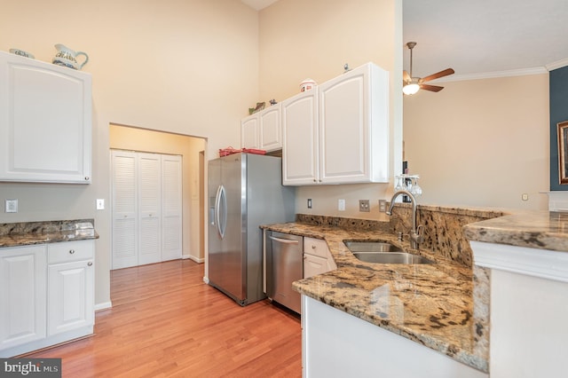 kitchen with stainless steel appliances, a sink, light stone counters, white cabinetry, and crown molding