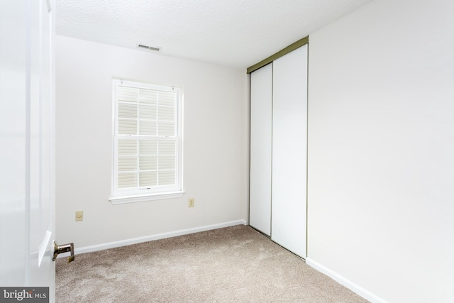 unfurnished bedroom with a textured ceiling, visible vents, baseboards, a closet, and light carpet