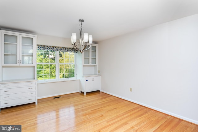 unfurnished dining area with an inviting chandelier, baseboards, and light wood finished floors