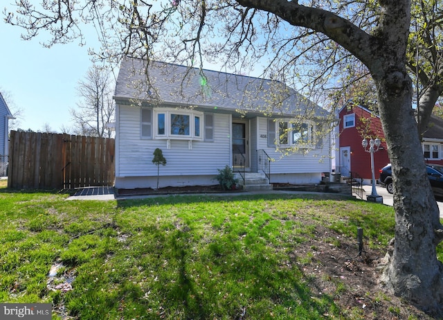 view of front of property with fence, roof with shingles, entry steps, and a front yard