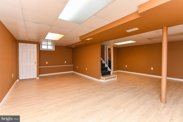 basement with light wood finished floors, a drop ceiling, visible vents, baseboards, and stairs