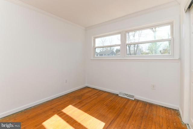 spare room featuring hardwood / wood-style floors, visible vents, baseboards, and ornamental molding