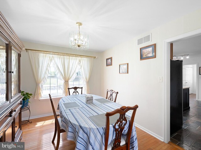dining space featuring wood finished floors, an inviting chandelier, rail lighting, baseboards, and visible vents