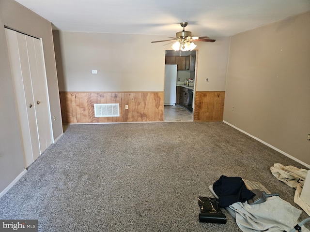 interior space with visible vents, ceiling fan, wooden walls, a wainscoted wall, and carpet