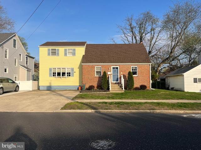 view of front facade featuring a front lawn, brick siding, a shingled roof, and concrete driveway