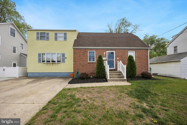 traditional-style house with roof with shingles, fence, a front lawn, and brick siding