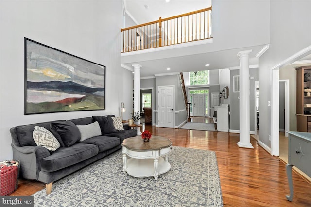 living room featuring decorative columns, visible vents, crown molding, a towering ceiling, and wood finished floors