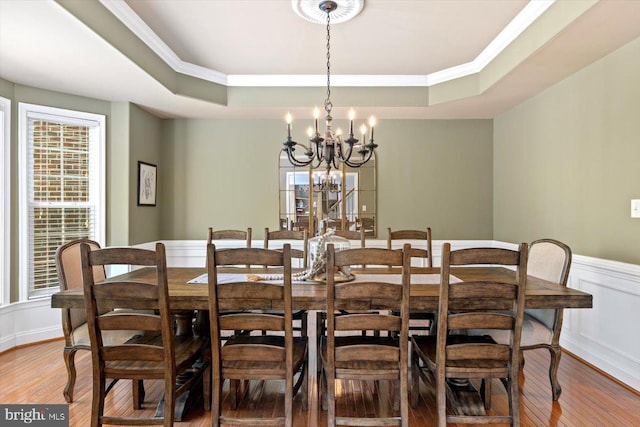 dining room with an inviting chandelier, a raised ceiling, crown molding, and wood finished floors