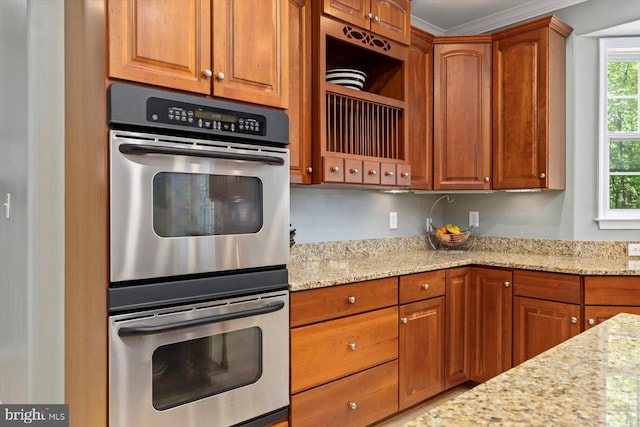 kitchen with light stone countertops, stainless steel double oven, ornamental molding, and brown cabinetry