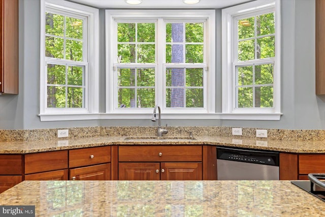 kitchen with a sink, light stone counters, stainless steel dishwasher, and brown cabinetry