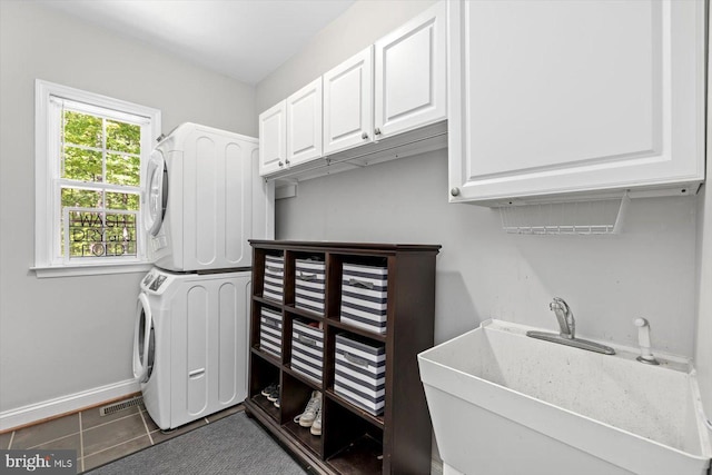 clothes washing area with dark tile patterned floors, stacked washer / dryer, cabinet space, a sink, and baseboards