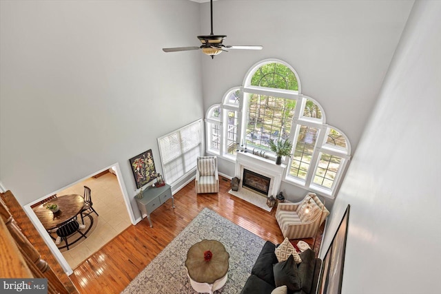 living area with ceiling fan, plenty of natural light, hardwood / wood-style flooring, and a towering ceiling