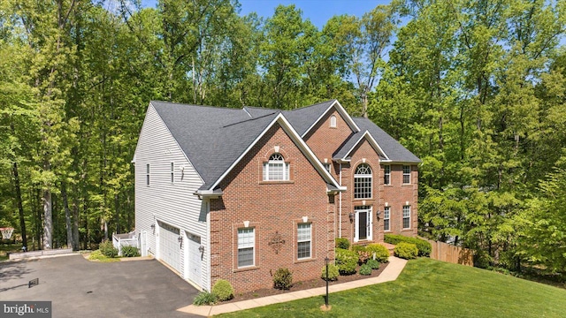 view of front facade featuring a front yard, a garage, brick siding, fence, and aphalt driveway