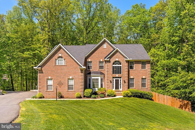 colonial house featuring brick siding, fence, and a front yard