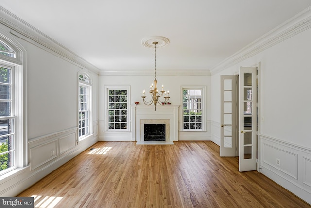 unfurnished living room with a wainscoted wall, ornamental molding, light wood finished floors, and a notable chandelier