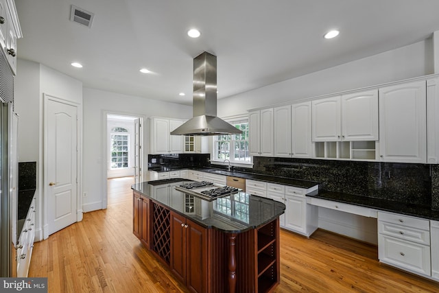 kitchen with open shelves, decorative backsplash, island range hood, a sink, and light wood finished floors