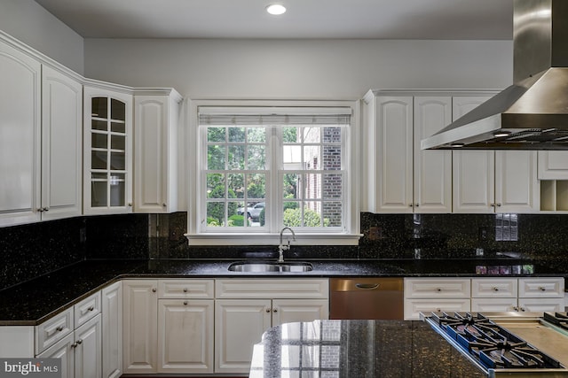 kitchen with glass insert cabinets, wall chimney exhaust hood, white cabinets, a sink, and stainless steel appliances