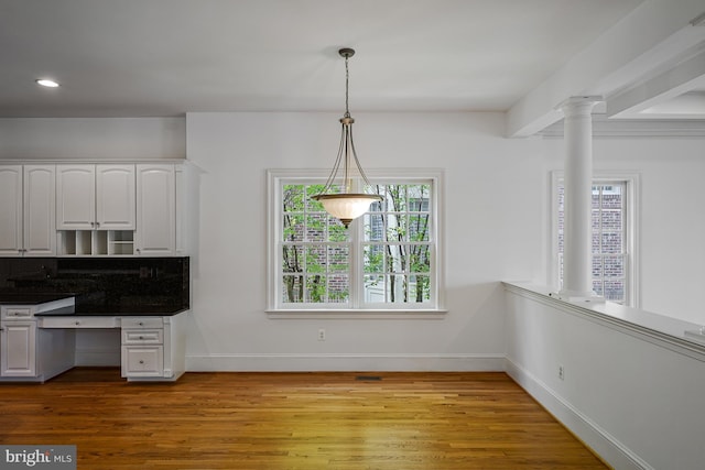 unfurnished dining area with ornate columns, baseboards, recessed lighting, and wood finished floors