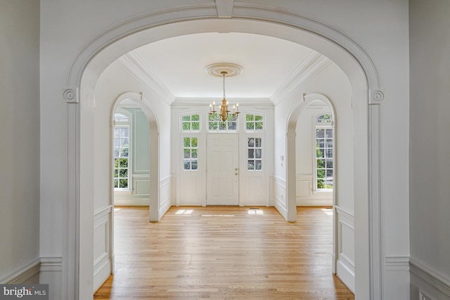 entrance foyer with arched walkways, a notable chandelier, light wood-style floors, ornamental molding, and a decorative wall