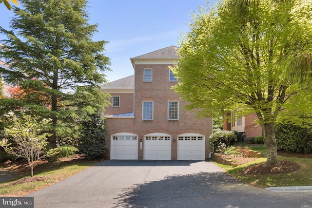 view of property with a standing seam roof, brick siding, driveway, and a garage