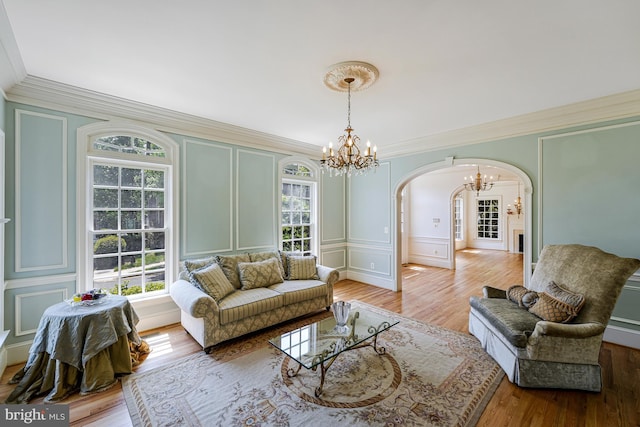 living area featuring arched walkways, a chandelier, ornamental molding, and a decorative wall