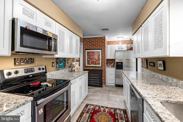 kitchen with white cabinets, light stone counters, visible vents, appliances with stainless steel finishes, and brick wall