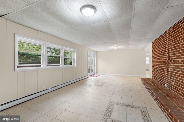 unfurnished room featuring a paneled ceiling, baseboards, brick wall, baseboard heating, and light tile patterned floors