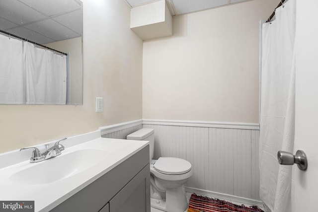 full bathroom featuring toilet, vanity, a drop ceiling, and wainscoting