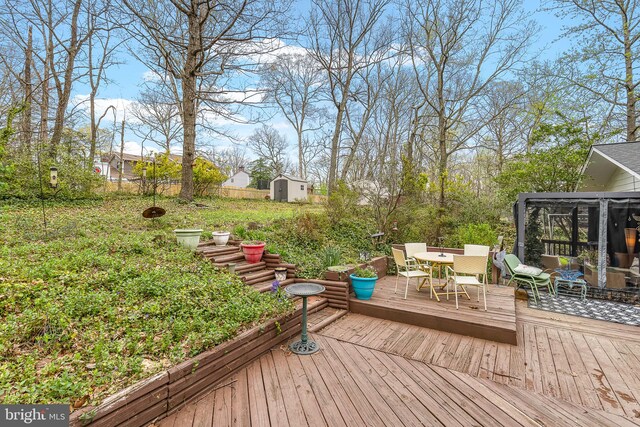 wooden deck featuring fence, an outbuilding, outdoor dining area, a storage unit, and a sunroom