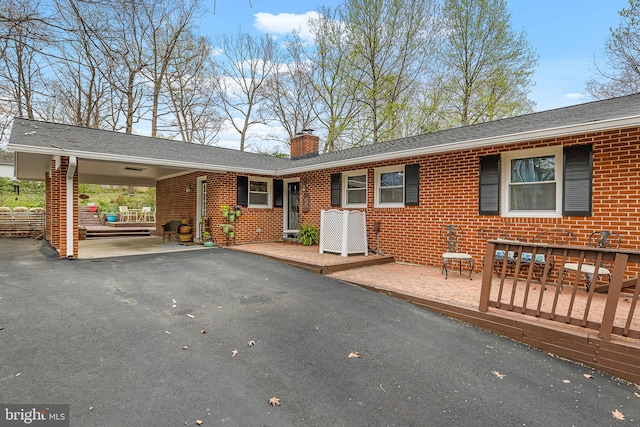 rear view of property featuring driveway, a chimney, brick siding, and an attached carport