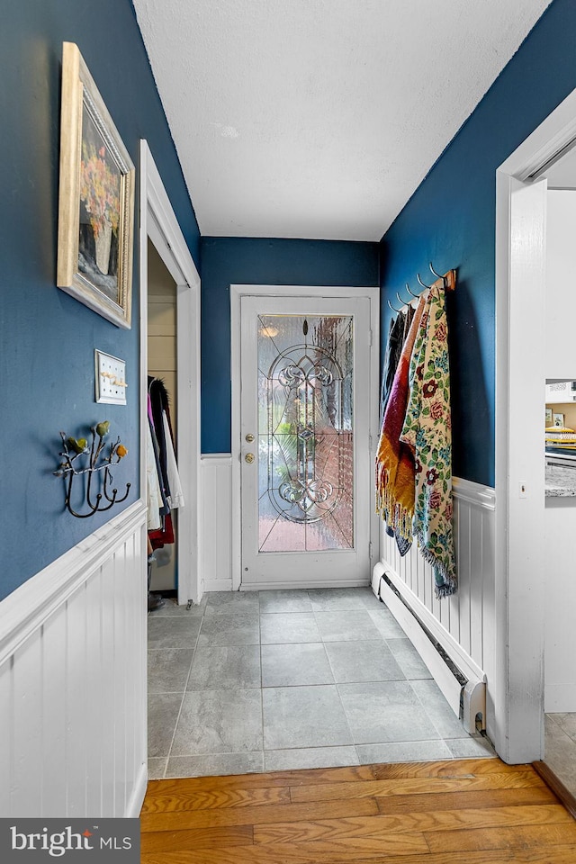 interior space with a baseboard heating unit, a textured ceiling, and wainscoting