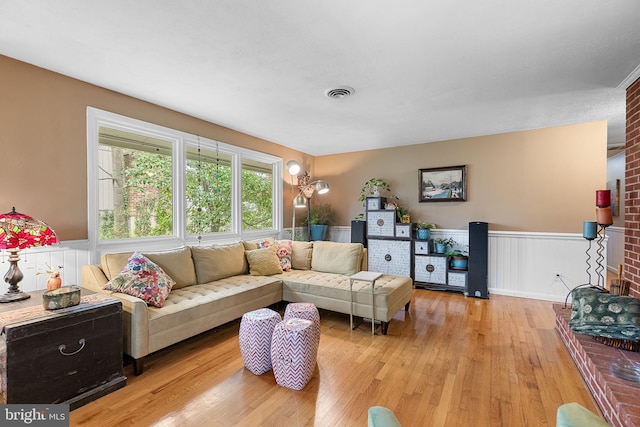living area featuring visible vents, light wood finished floors, and a wainscoted wall